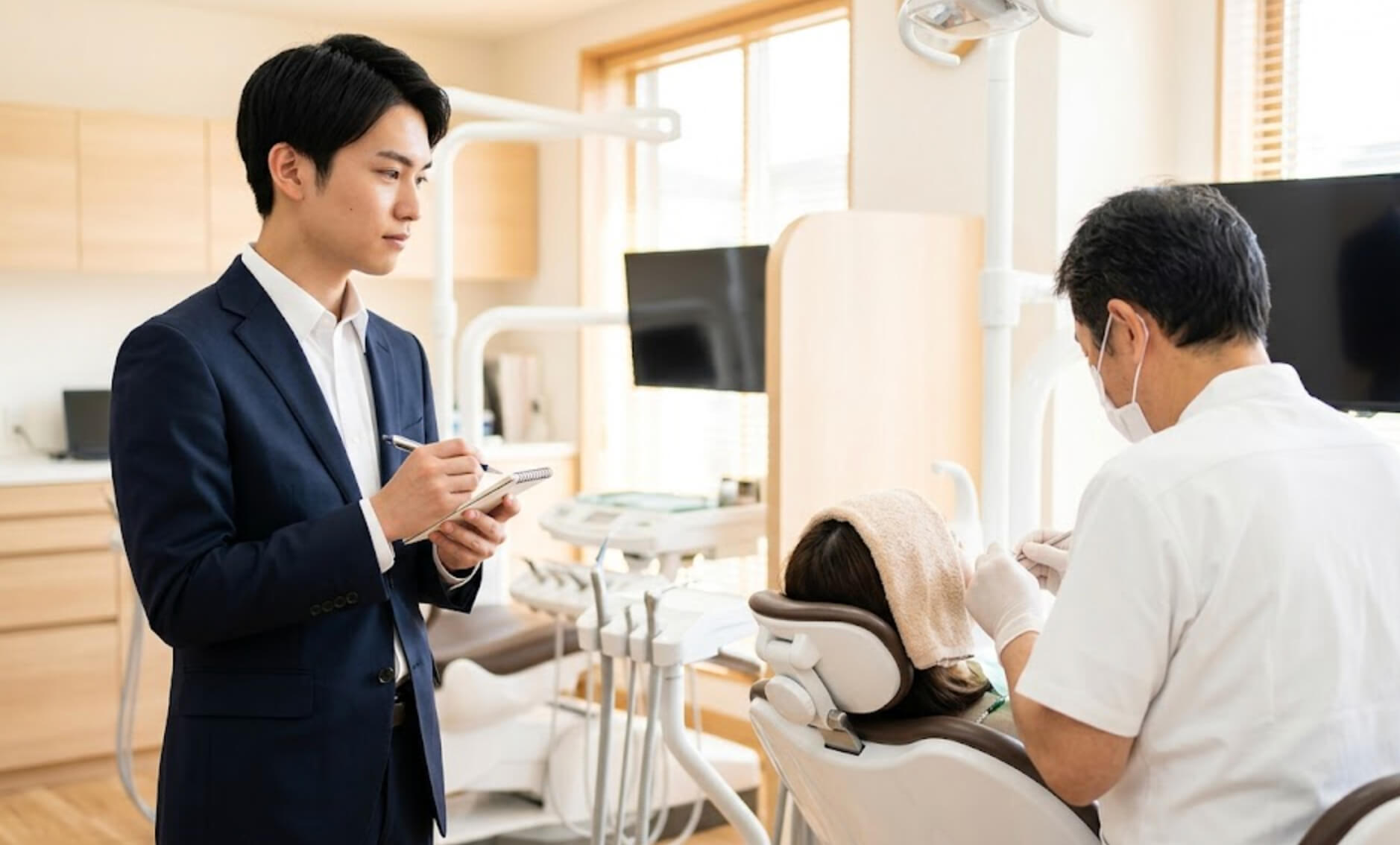 歯科医院の見学で、診療の様子を真剣に観察しながらメモを取る新卒生の男性の様子